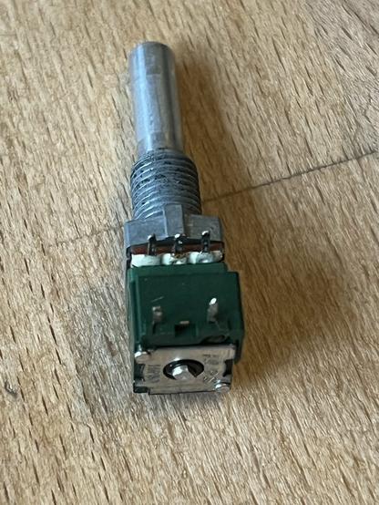 Drehpotentiometer mit grünem Gehäuse und metallener Front und Achse. Zu sehen sind die Anschlüsse und die Beschriftung auf der Rückseite ALPS Japan