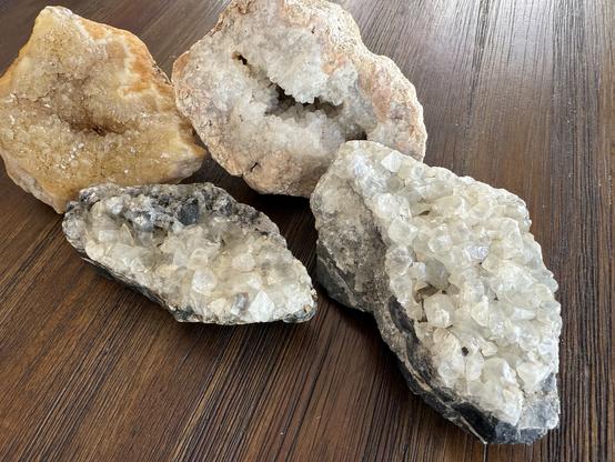 Four geodes. Two are white crystals formed on dark granite, the other two are encased in yellow/pink rock.