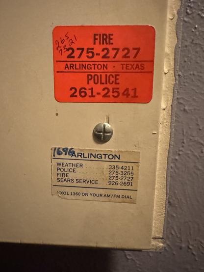 Two old stickers on the inside of a cabinet with numbers for fire, police, weather, and of course Sears - which predates 911 adoption.
