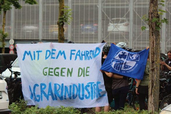 Foto vor einem Parkhaus mit einem Transpi "Mit dem Fahrrad gegen die Agrarindustrie"