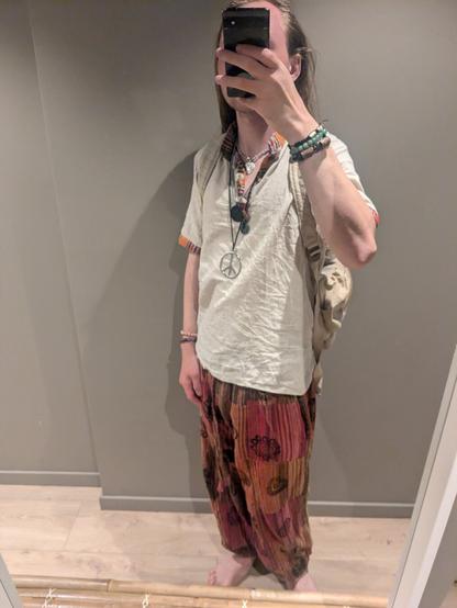 The individual is indoors, taking a selfie in front of a mirror. In the background, there's a plain wall and wooden structure on the floor, adding a minimalistic touch to the setting.