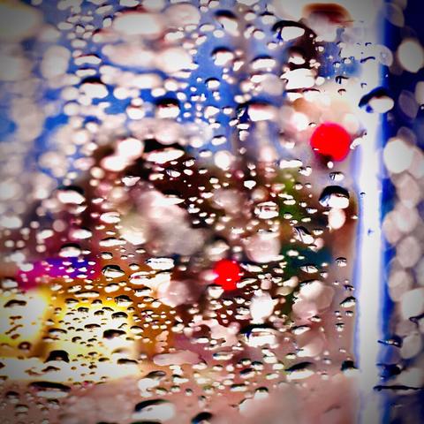 Bright red, yellow, and blue lights of different shapes and sizes are viewed out of focus through a window covered in raindrops.