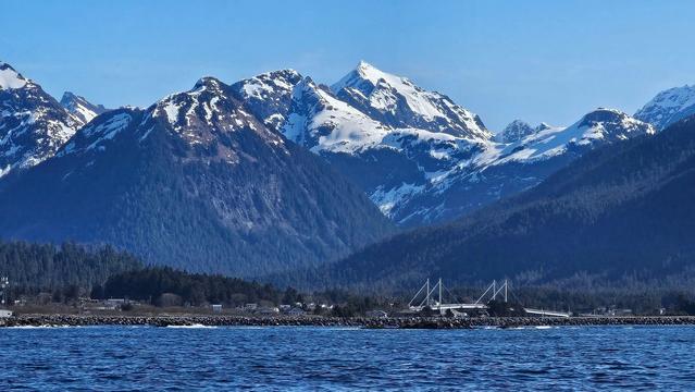 Bright blue ocean at the bottom of the pic, a gravel lined spit (the airport runway) is next, then the bridge that links Baranof and Japonski Islands. A thin strip of Sitka, then huge, towering, snow capped mountains dwarf all, with clear blue skies finishing the scene.