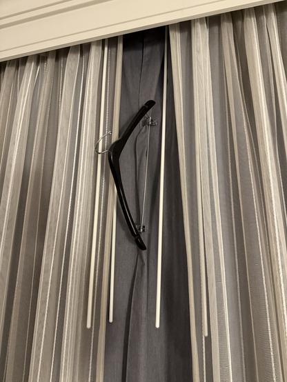 A hotel room window with the blinds held shut using the trouser clips of a clothes hanger.