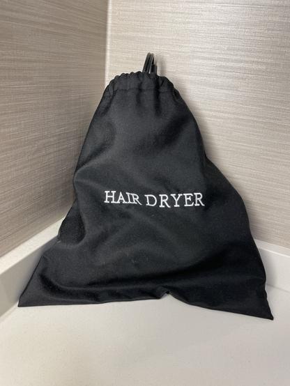 a black nylon-canvas drawstring bag with the words "HAIR DRYER" embroidered on it in all caps white text with serifs