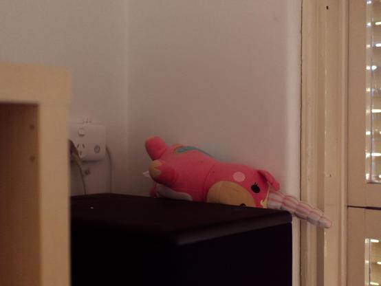 A stuffed "balloonicorn" toy has fallen down, partially, by a speaker and a wall.