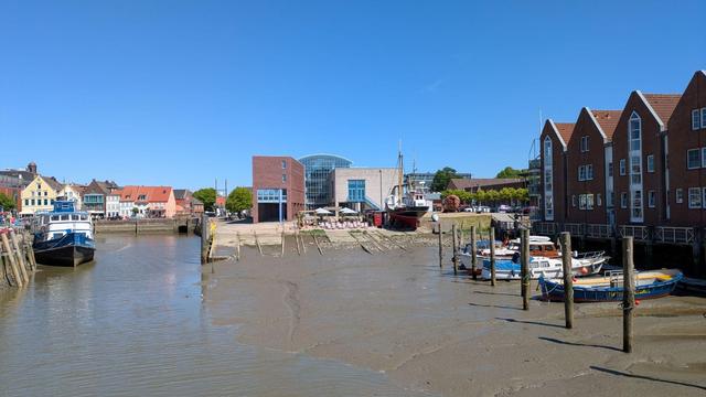 Hafen bei Niedrigwasser mit Booten rechts und links, hinten eine alte Slipanlage (mit Cafe davor!) und ein aufgebocktes Museumsschiff