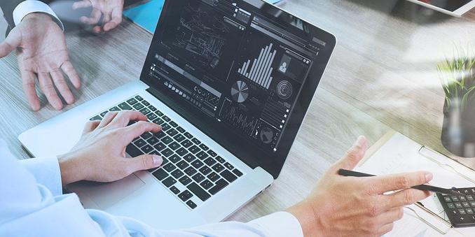 A stock image of a lot of data - charts, graphs, etc - on a laptop screen. Two pairs of hands are visible, suggesting two people are discussing the data.