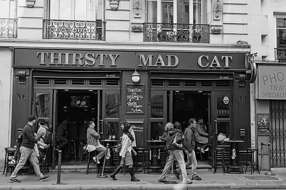 B&W shot of people passing in front of the Thirsty Mad Cat, a bar in Paris