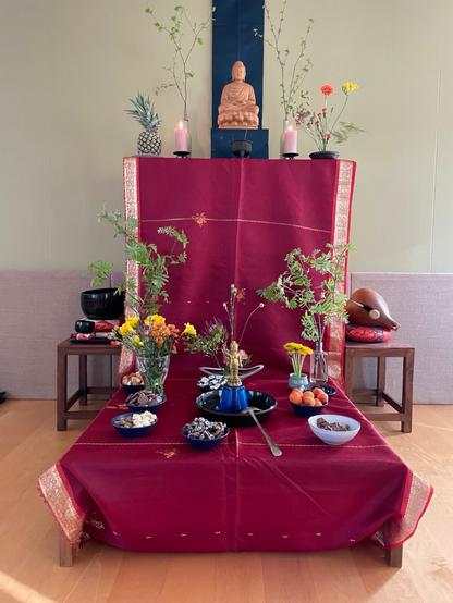Koristeltu Buddha-alttari. Alhaalla keskellä on lapsi-Buddha teealtaassa. Ympärillä ruokauhreja, hedelmiä, pähkinöitä ja karkkeja ynnä muuta. Useita kukka-asetelmia ja vehreitä oksia.