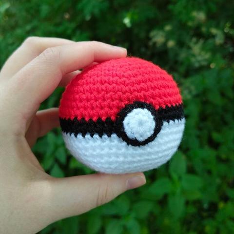 A picture of a white hand holding a crocheted amigurumi pokeball.
