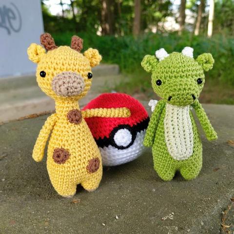 A picture of a crocheted giraffe, dragon and pokeball all posing together.