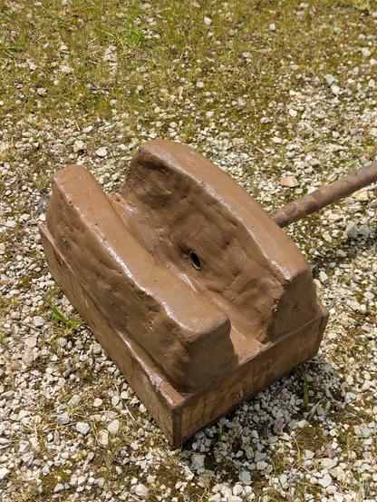 Posée au sol sur des graviers a l'extérieur. Une petite caisse en bois 25x35x12. Et une deux sortes de lèvres courbes de 15cm de haut, en argile qui constituent le foyer. On voit le tuyau de la tuyère qui dépasse a l'intérieur.
