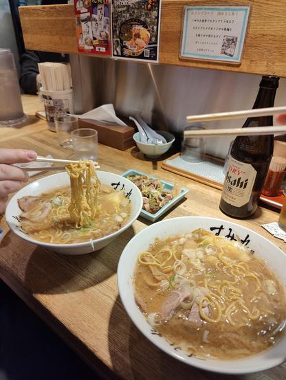 A photo of two bowls of ramen with a bottle of Asahi Super Dry beer.
