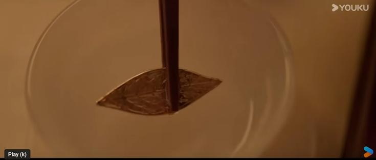 Metal leaf lifted from liquid with chopsticks.