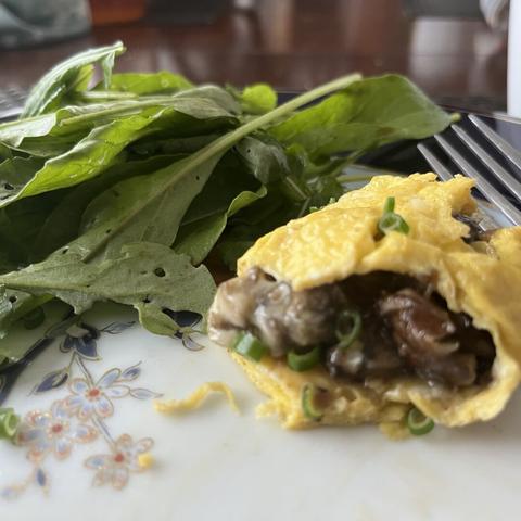 Close up of the omelet filled with chopped, sautéed mushrooms onions, next to the arugula and the tines of a fork