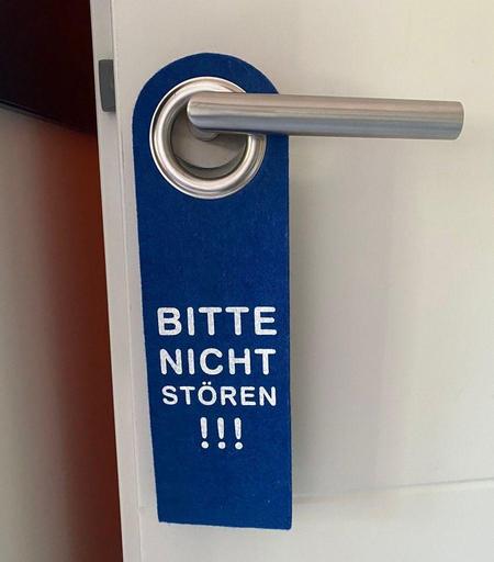 A blue door hanger on a door, reading a text in German that can be translated to: Do not disturb!!!