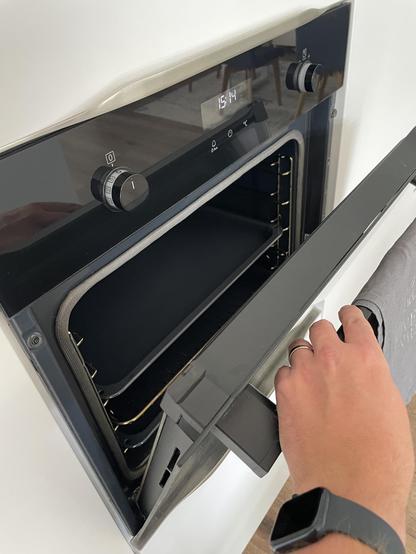 A hand opening an oven using the towel rail (also known as oven door handle)