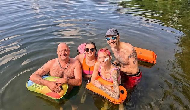 The four of us in the lake in our swimming cozzies and holding our tow floats. Hope has a medical feeding tube in her nose, but we’re all smiling and looking very happy about life. And this was before our sauna.