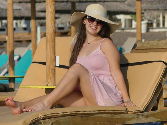 Emily Grice lounging in a pink dress and sun hat, #barefoot on a beach chair modeling on her first day of her grand tour of Europe.