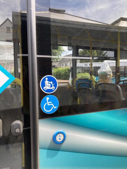 Zeigt die Seite des Busses an der hinteren Tür. Aufkleber Mobilitätsroller, darunter Aufkleber Rollstuhl,