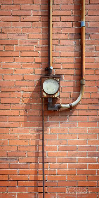 An old, rusty electric meter base and conduit on a brick wall.