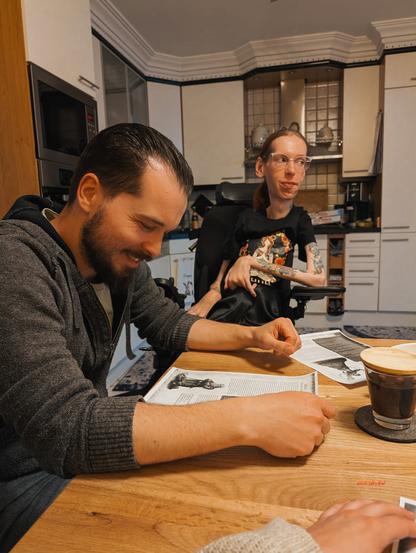 Chris und ich sitzen nebeneinander an meinem Küchentisch. Vor uns liegen die Charakterbögen unserer DSA-Charaktere. Chris lächelt und betrachtet seinen Charakter, ich schaue etwas skeptisch nach rechts in Richtung unseres Gamemasters.