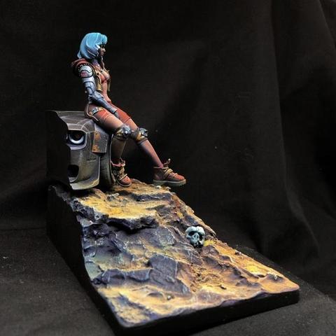 This miniature scene is an evocative diorama that tells a story of solitude, resilience, and perhaps a touch of melancholy. The woman has an angular, dynamic pose, leaning slightly backward as she rests on the machine. Her blue hair is vivid and eye-catching, a contrast to the otherwise muted and earthy tones of the diorama. She wears a mix of battle-worn armor and sleek futuristic attire, with details such as metallic knee guards and reinforced boots suggesting a life of survival and action. Her expression, though subtle, conveys introspection, as if she’s lost in thought or recovering after a long journey. The mechanical relic she’s seated on — possibly the remains of a robot — features a single visible, lens-like eye that stares blankly into the void, a haunting reminder of technology's downfall.
