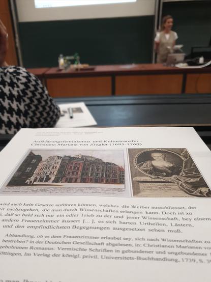Foto des Handouts (darauf zwei zeitgenössische Abbildungen, eine davon von C. M. v. Ziegler sowieso Zitate), dahinter unscharf Blick in Richtung Tafel / Präsentationswand und auf die Dozentin.