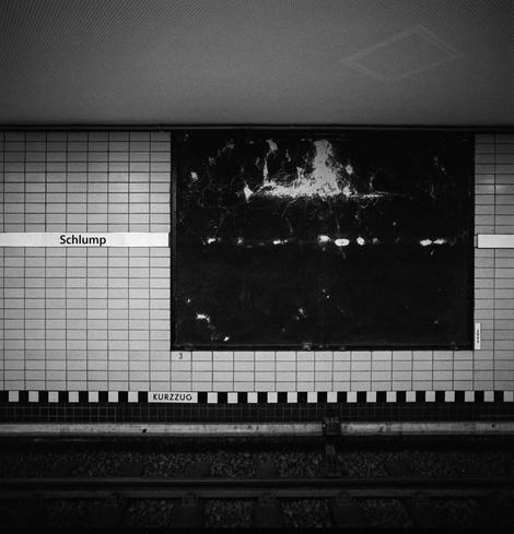 black and white photograph across the U-bahn tracks at the station Schlump. a vacant billboard is black with white highlights.