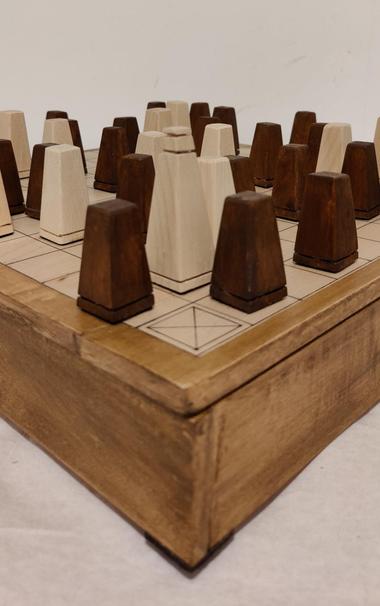 A close up of the corner of a hand made hnefatafl / viking chess set. Dark and light pieces sit atop a two colour box on the top of which is a playing surface for the game.