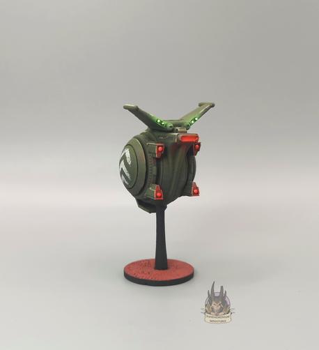 Drone - it's spherical with stablising fins at the top, in a drab green with grey chevron patterns on the side panels -back right view