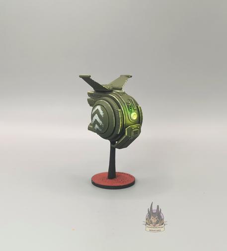 Drone - it's spherical with stablising fins at the top, in a drab green with grey chevron patterns on the side panels - front left view