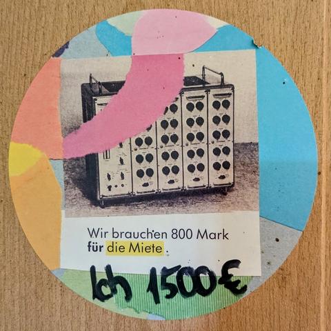 Das Bild zeigt einen Aufkleber. Der Aufkleber ist recht bunt, darunter rosa, blau, gelb und grün. In der Mitte des Zettels befindet sich ein Schwarz-Weiß-Foto eines alten, großen elektronischen Geräts mit vielen Knöpfen und Schaltknöpfen. Unter dem Foto steht in schwarzer Schrift: "Wir brauchen 800 Mark für die Miete." Darunter, in großer, schwarzer handgeschriebener Schrift, steht "Ich 1500€".