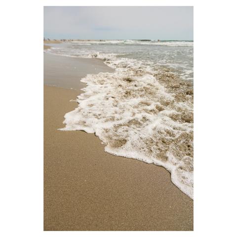 Wide angle shot taken on a beach. A foamy wave is rolling in from the right. The sky is cloudy.