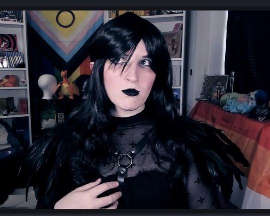 Foto von Lili stark verkleidet als ihr Vampire Charakter: Elisabeth von Rabenschrei. Sie trägt ein schwarzes Kleid mit schwarzen Federschulterepauletten, eine schwarze Perücke mit Locken, schwarzen Lippenstift und dramatisch silbernes Augenmakuep. Sie guckt genervt hoch.