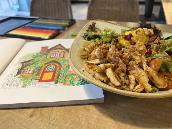 Fast fertig ausgemalte Seite eines Ausmalbuches, ein Holzhaus im Grünen mit roten Fenstern und Türen.

Daneben eine lecker gefüllte Bowl mit viel Gemüse und Hähnchen Fleisch Streifen