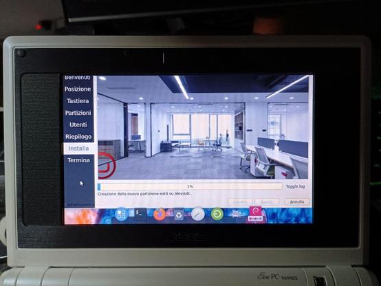 L'immagine mostra uno schermo di un laptop ASUS Eee PC Series in fase di installazione di un sistema operativo. Sullo schermo, si vede una finestra di installazione con un menu a sinistra che contiene le opzioni "Benvenuti", "Posizione", "Tastiera", "Partizioni", "Utenti", "Riepilogo", "Installa" e "Termina". La barra di progresso mostra che la creazione di una nuova partizione ext4 su /dev/sde sta avvenendo al 1%. Sullo sfondo, è visibile un'immagine di un ufficio moderno con sedie, tavoli e finestre che lasciano entrare la luce naturale. In basso, si notano icone di applicazioni come "Iniziare", "Recycle Bin", "Clock" e altri.