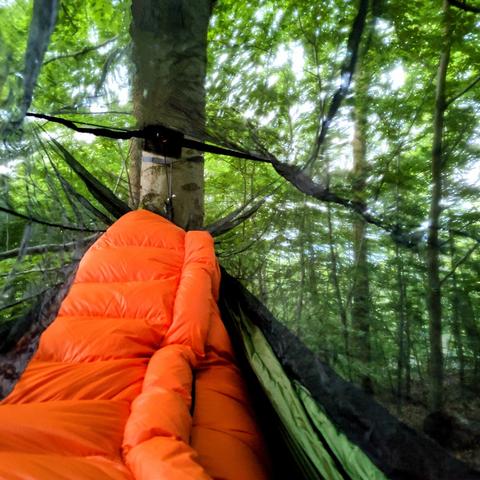 Das Fußteil eines orangen Schlafsackes in einer Hängematte im Wald.