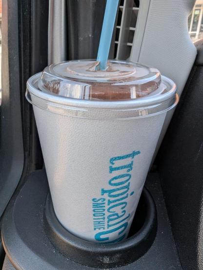 Large to go cup with cap and straw with tropical smoothie cafe logo in car cup holder.