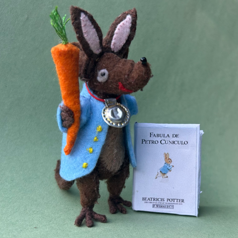 Photo of Silvius the little Latin mouse, dressed as Peter Rabbit with bunny ears and a blue jacket. He has a miniature copy of the Latin translation from 1962 of the Beatrix Potter classic.