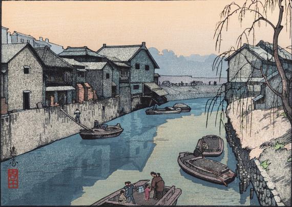 A view from the Iidabashi, looking down the curve of the Kanda River. Wooden boats clutter the waterway; in the foreground, a female figure on a boat is surrounded by young children, not all of whom are behaving themselves. Beyond, two figures in two different boats hold a conversation; further on, others are offloading merchandise, carrying items out of a boat, up a narrow ramp and into a riverside warehouse. On our right, a willow tree is just beginning to show new leaves; above, the sky is grimy and overcast.