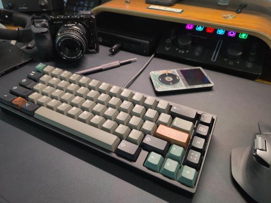 My black neo65 mechanical keyboard on my black (faux) leather deskmat surrounded by a screwdriver, a transparent iPod classic, my Sony camera and my mouse.