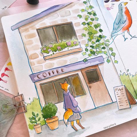 Photo of a watercolor sketchbook. The drawing is an anthropomorphic fox looking at a cafe building. The building has plants outside, a planter box in the top window, and ivy on the side of the wall.