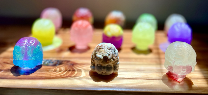 Colorful resin casts of an old doll head with original in focus front and center