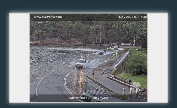 Webcam of road across weir going underwater, three utes nonetheless plowing across.