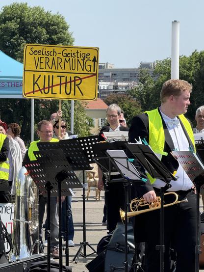 Blechbläser, dahinter Demoschild: Ortsausgang „Kultur“, was folgt „seelisch-geistige Verarmung