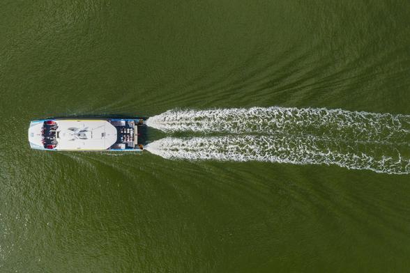 A CityCat, from directly above, moving on the Brisbane River, with its wake extended behind it
