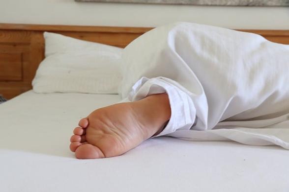 foot peeking out from white sheets on a bed as the person sleeps