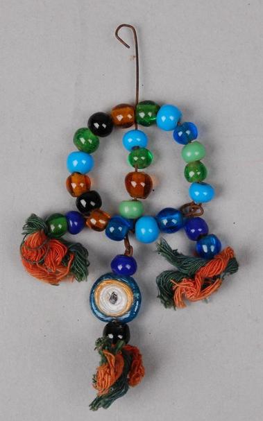 From 1960s Hebron, Palestine, a beaded amulet in circular form 

Created from plain blue, green, amber and black glass beads threaded onto wire which has been bent at the top to form a hook 

Three beaded pendants hang from the circle, each pendant has a tassel made from red and green cotton thread 

In addition, the centre pendant has a single blue, yellow and white glass bead in the form of an eye, used to ward off the 'eye of envy' 

Length: 14.30cm, Weight: 24g, Width: 8.20cm

Source : The British Museum, Accession Number As1966,01.835 

#BeadSocietyGB #Beads #HistoryOfBeads #WestBank #Hebron #Palestine #BritishMuseum #Amulet #EyeOfEnvy